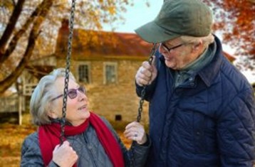 A picture of an elderly couple sitting on a swing and looking at each other